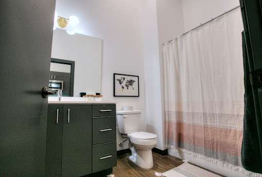 Modern bathroom with dark vanity and white shower curtain at The Traveler Apartments, Omaha, 68131