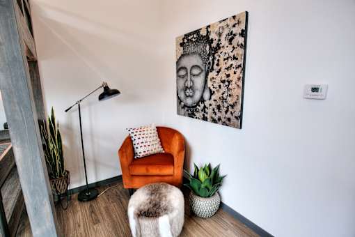 Cozy reading nook with orange chair and buddha artwork at The Traveler Apartments, Omaha
