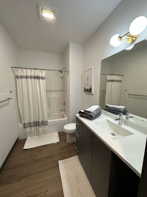 Bathroom with dark wood vanity and tub shower combo at The Traveler Apartments, Omaha, NE 68131