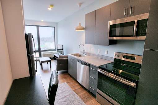 Modern kitchen with gray cabinetry and dining area at The Traveler Apartments, Omaha, NE 68131