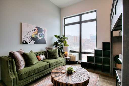 Living room with green sofa and large window at The Traveler Apartments, Omaha, NE 68131