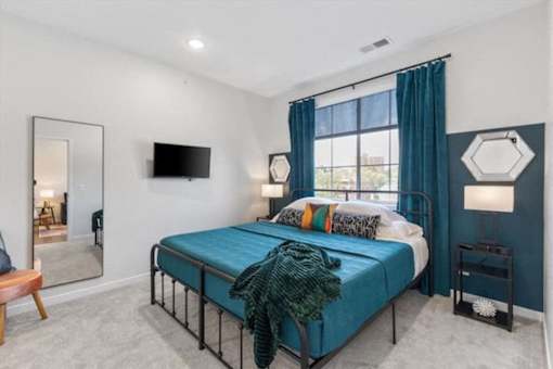 A bedroom with a bed, a mirror, a television, and a window with curtains.