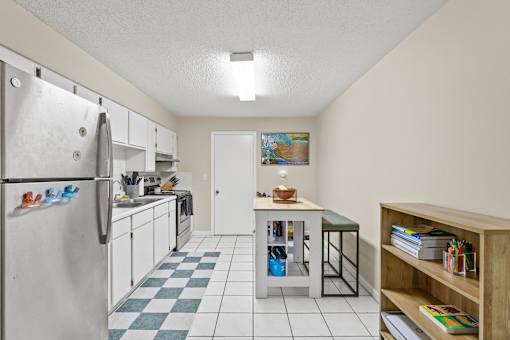 A kitchen with a refrigerator, a table, and a bookshelf.