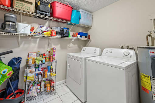 A laundry room with two washing machines and a shelf with various items.