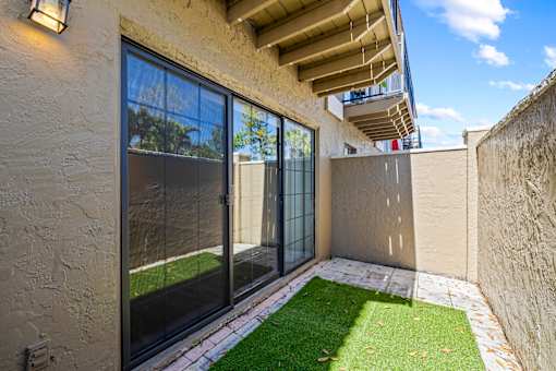 A patio with a glass door and a small lawn.