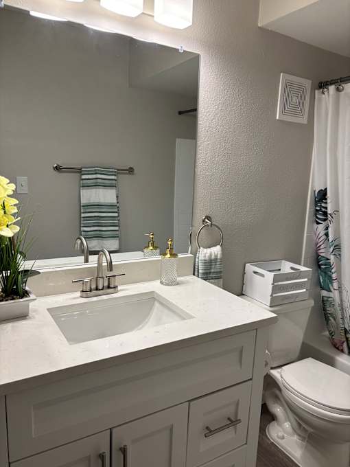 A white bathroom with a sink, toilet, and a mirror.