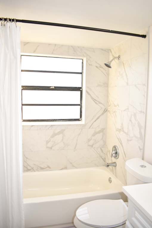 A white toilet sits next to a bathtub in a bathroom with a marble wall.
