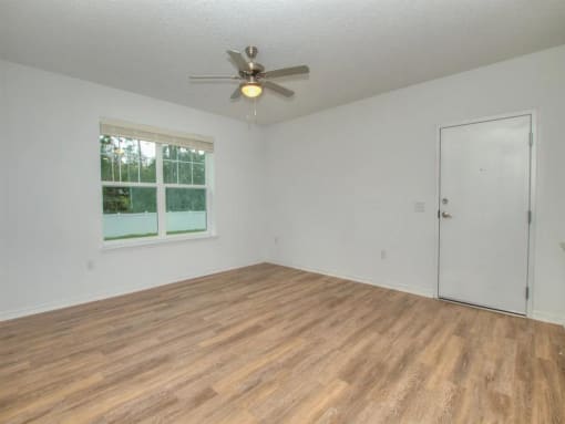 an empty living room with a ceiling fan and a window