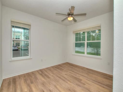 an empty living room with a ceiling fan and two windows