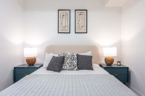 A bedroom with a large bed, two nightstands with lamps, and two framed artworks on the wall.