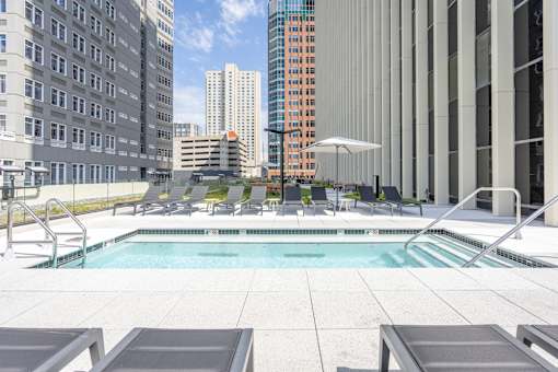 A pool surrounded by lounge chairs and umbrellas in a city setting.