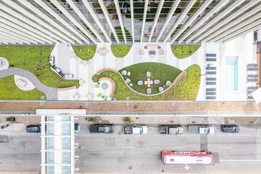 A green and white park area is surrounded by a parking lot and a building.