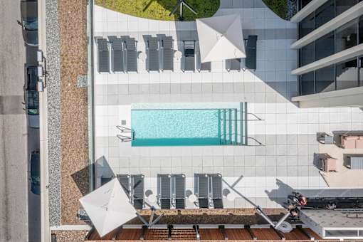 A modern building with a pool and sun loungers.