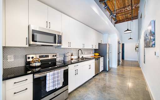 A modern kitchen with white cabinets and black countertops at Judson Mill Lofts, Greenville, 29611