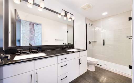 A modern bathroom with a large mirror, sink, and glass shower stall at Judson Mill Lofts, Greenville, South Carolina