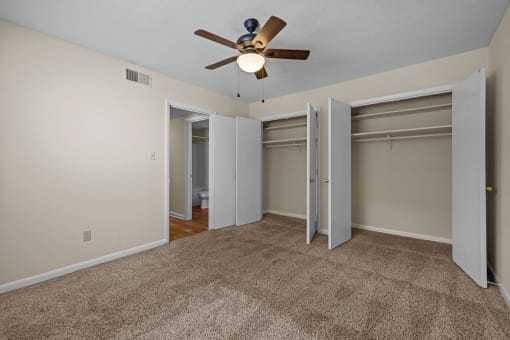 an empty living room with a ceiling fan and two closets