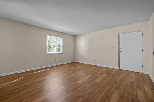 the spacious living room of an empty home with wood flooring and a window