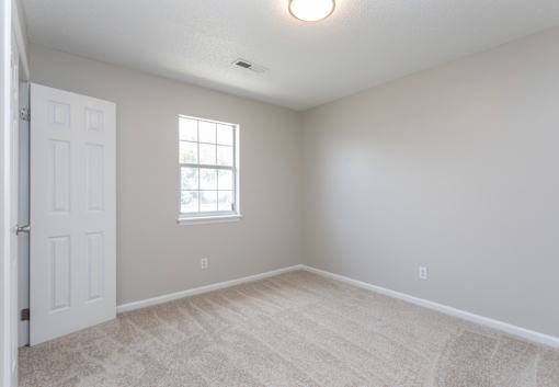 A room with a carpeted floor, a window, and a door.