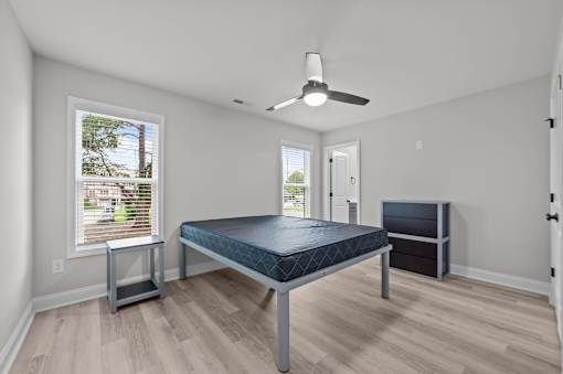 A room with a bed, a fan, and a window with blinds.