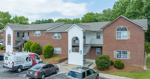 A white two story apartment building with a red brick exterior and a white van parked in front.