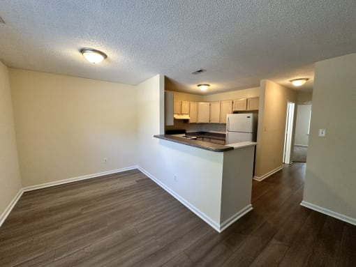 an empty living room and kitchen with a counter top and a refrigerator