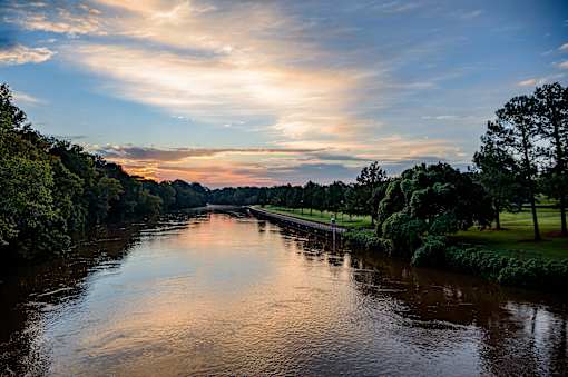 A serene river flows through a lush green landscape under a sky painted with hues of sunrise or sunset.
