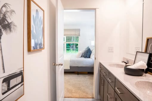 A bathroom with a sink, mirror, and a bedroom in the background.