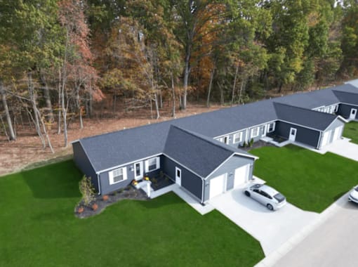 A large house with a grey roof and white trim is surrounded by a green lawn and trees.