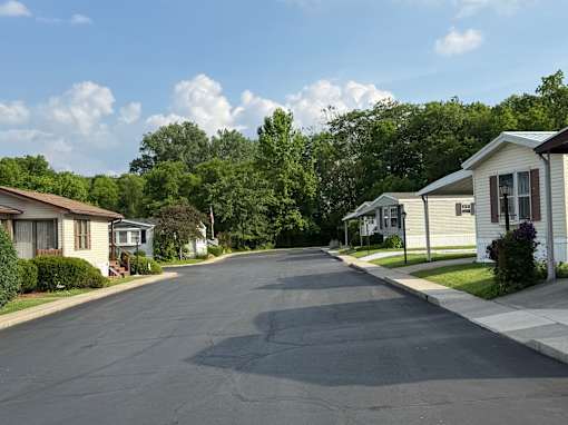 A residential street with houses on both sides and trees in the background.