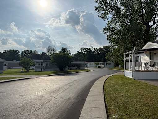 A residential street with trees and houses on both sides under a sunny sky.