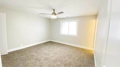 A room with a carpeted floor, a ceiling fan, and a window.