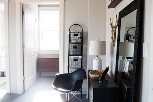 A black chair sits in a white room with a black mirror and a black shelf.