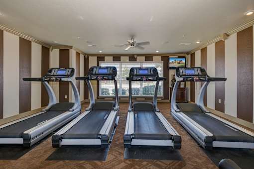 a gym with four treadmills and a ceiling fan