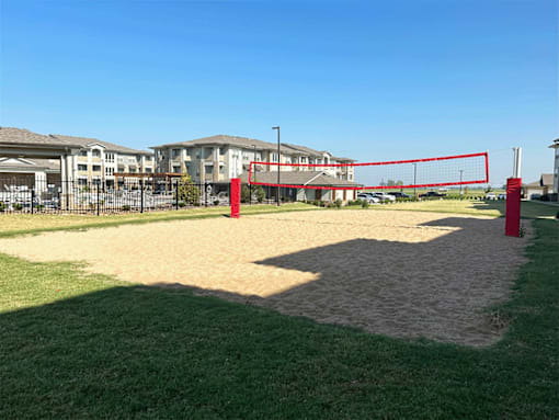 a sandy volleyball court in a grassy area with houses in the background