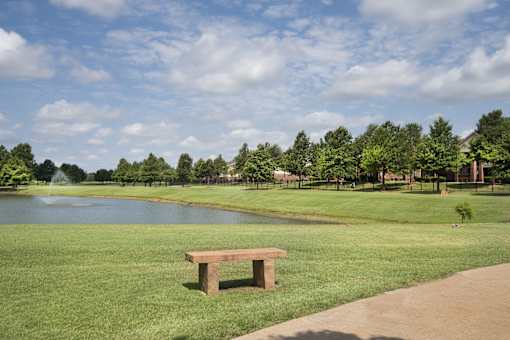 A park bench sits on a grassy area next to a pond.