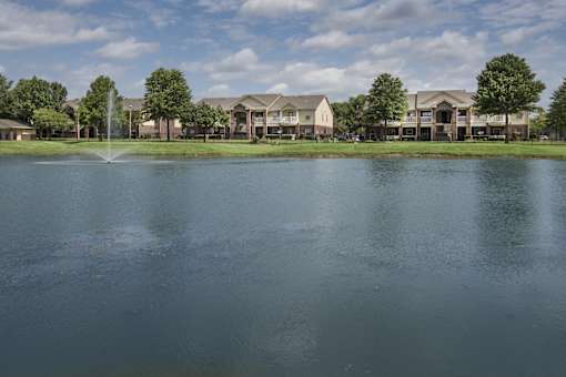 A fountain in the middle of a lake in front of apartment buildings.