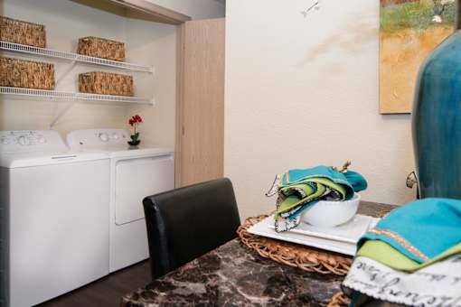 A laundry room with a washer and dryer, a black chair, and a table with a bowl and a bag on it.