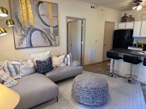 A living room with a grey couch, a grey ottoman, and a painting on the wall.