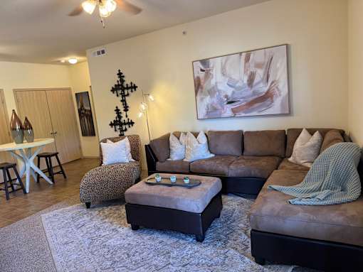A living room with a brown couch, a grey ottoman, and a painting on the wall.