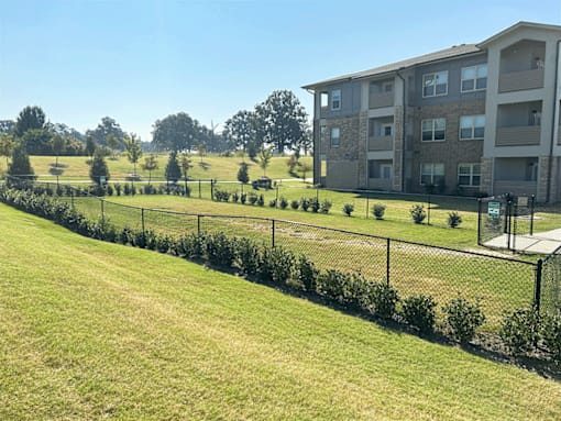 A grassy field with a fence and a building in the background.