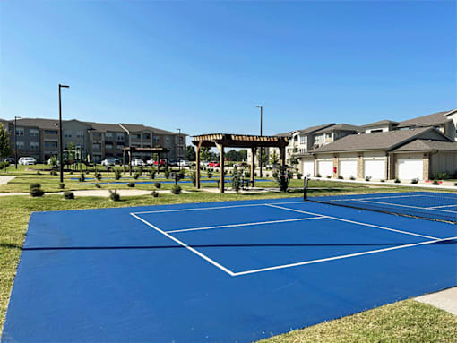 A blue tennis court in the middle of a grassy area with a building in the background.