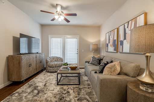 A living room with a grey couch, a wooden cabinet, a ceiling fan, and a rug.