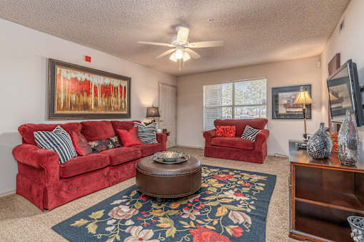 a living room with red couches and a rug and a ceiling fan