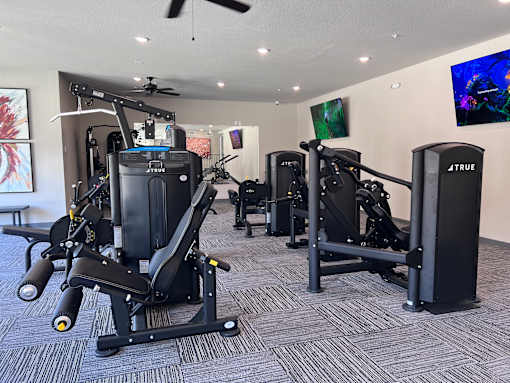 A gym with a variety of equipment including a squat rack, a leg press machine, and a bench press.