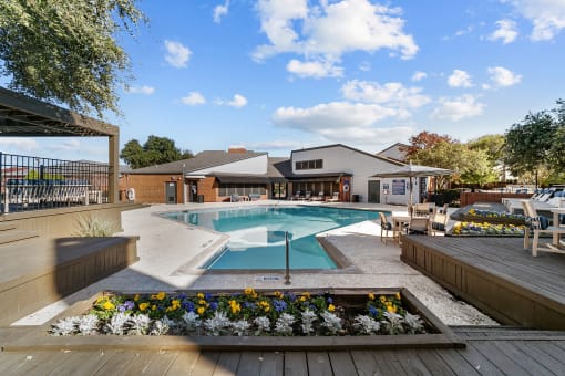 a swimming pool with patio furniture and flowers in front of a house
