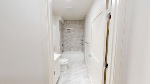 A white bathroom with a marble tiled shower.