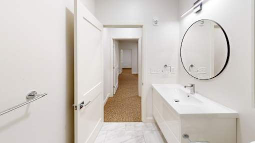 A white bathroom with a round mirror and a white sink.