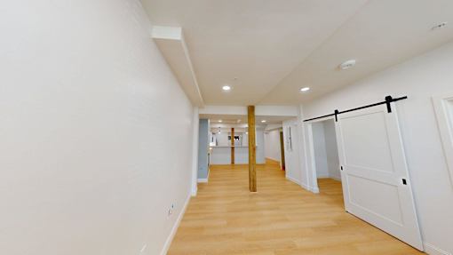 A long hallway with a white wall and a wooden floor.