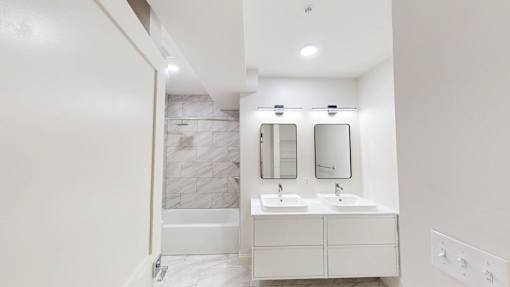 A white bathroom with a marble tile shower and a double sink vanity.