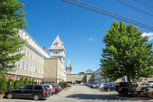 A street view of a building with a tower and cars parked on the side.